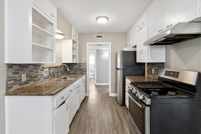 kitchen with light wood-type flooring, dark stone counters, sink, white cabinets, and stainless steel range with gas cooktop