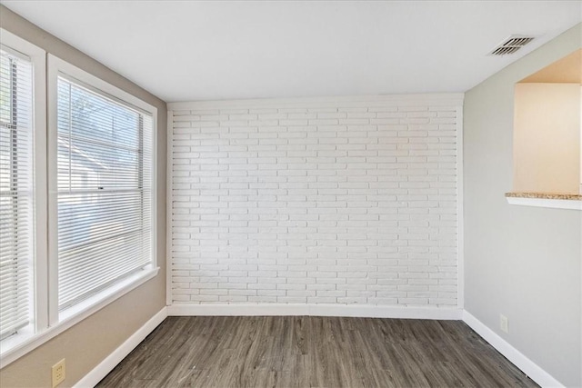 empty room featuring dark hardwood / wood-style floors, a healthy amount of sunlight, and brick wall