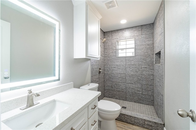 bathroom featuring hardwood / wood-style flooring, vanity, toilet, and a tile shower