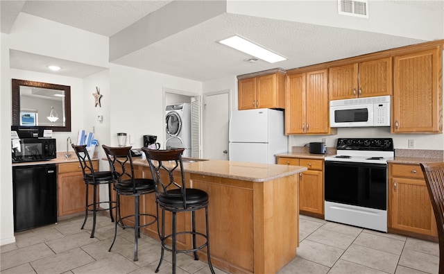 kitchen with a kitchen bar, light stone counters, a textured ceiling, black appliances, and stacked washer and dryer