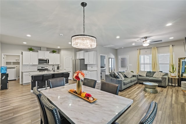 dining area featuring ceiling fan with notable chandelier, washer / dryer, light wood-type flooring, and sink