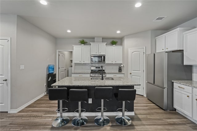 kitchen with a center island with sink, sink, hardwood / wood-style flooring, light stone countertops, and stainless steel appliances