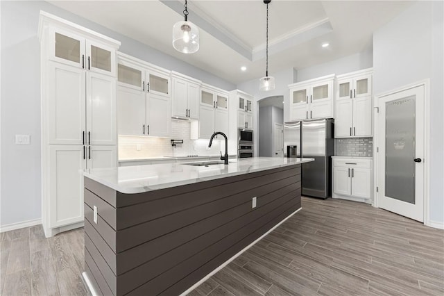 kitchen with sink, hanging light fixtures, a center island with sink, appliances with stainless steel finishes, and a tray ceiling