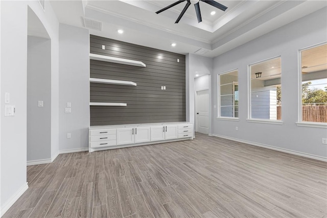 unfurnished living room featuring ornamental molding, wooden walls, a raised ceiling, ceiling fan, and light hardwood / wood-style floors