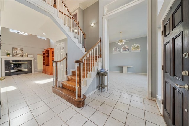 foyer featuring a premium fireplace, crown molding, light tile patterned flooring, and ceiling fan