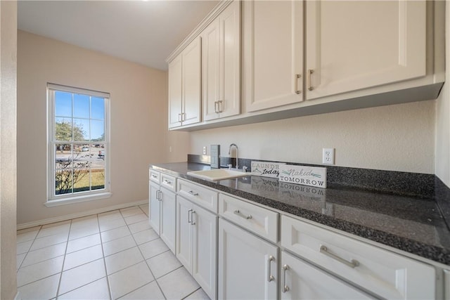 kitchen with white cabinetry, sink, light tile patterned floors, and dark stone countertops