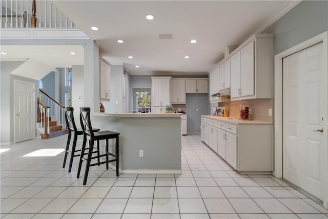 kitchen featuring ornamental molding, a breakfast bar, light tile patterned floors, and white cabinets