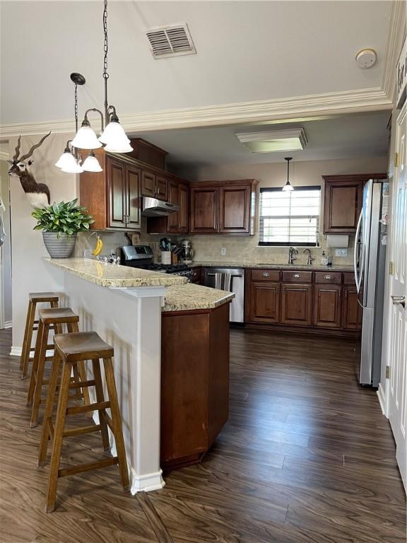 kitchen with appliances with stainless steel finishes, visible vents, dark wood-style floors, under cabinet range hood, and a peninsula