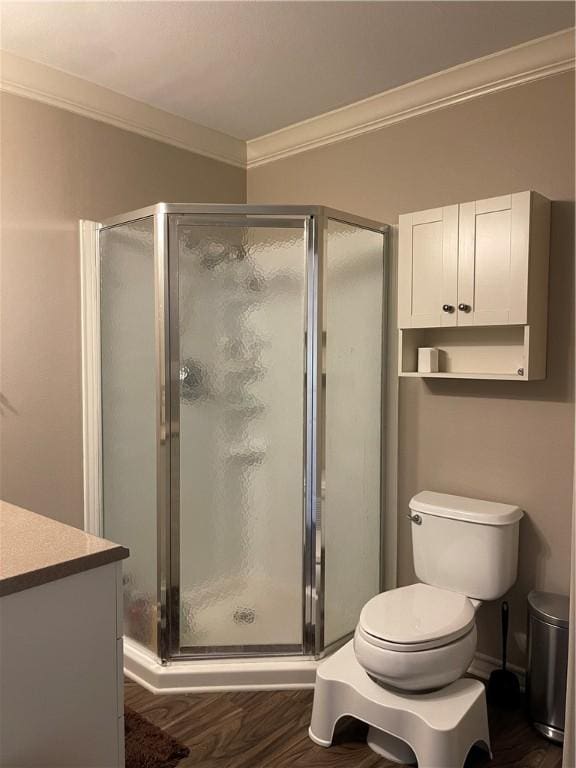 bathroom with wood finished floors, toilet, a stall shower, and crown molding