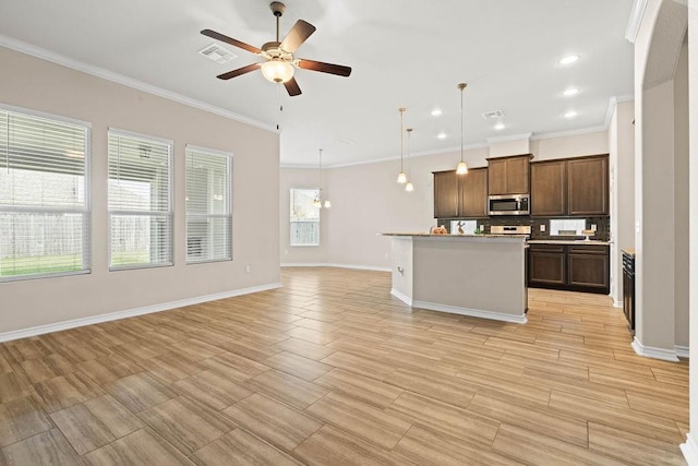 kitchen featuring hanging light fixtures, tasteful backsplash, a kitchen island with sink, ceiling fan, and ornamental molding