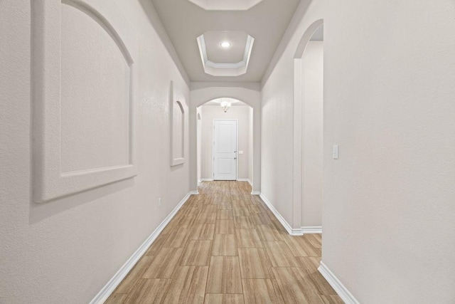 hallway with light wood-type flooring, crown molding, and a tray ceiling