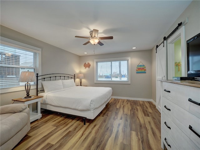 bedroom with a barn door, hardwood / wood-style flooring, and ceiling fan