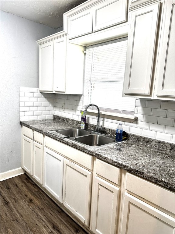 kitchen featuring sink, dark hardwood / wood-style floors, dark stone countertops, tasteful backsplash, and white cabinetry