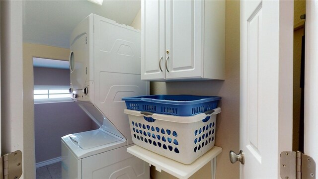 washroom with baseboards, cabinet space, and stacked washer / drying machine