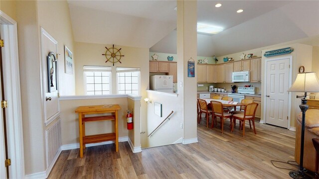 kitchen with light brown cabinets, white appliances, baseboards, lofted ceiling, and light wood-type flooring