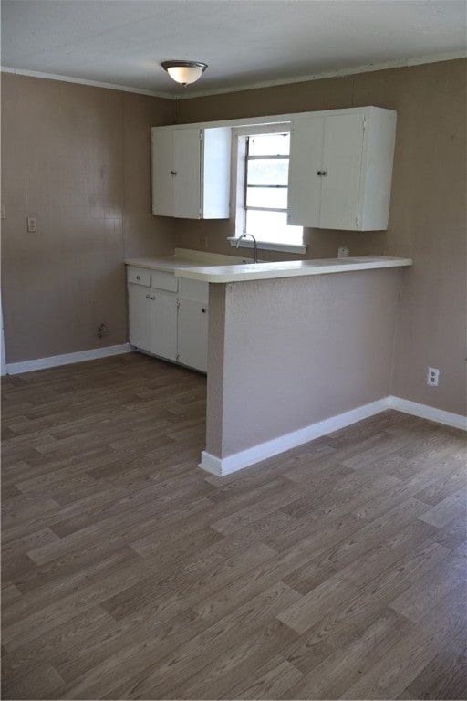 kitchen featuring white cabinets, ornamental molding, kitchen peninsula, and hardwood / wood-style floors