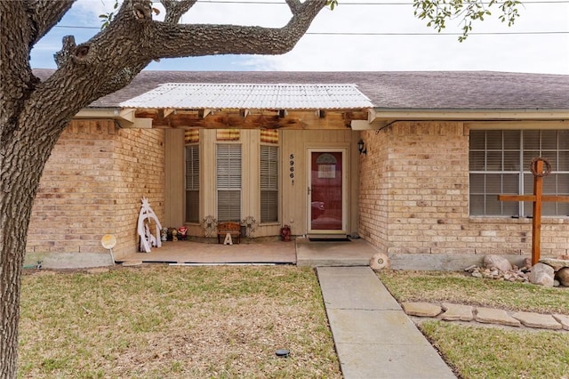 property entrance with brick siding, a lawn, and roof with shingles