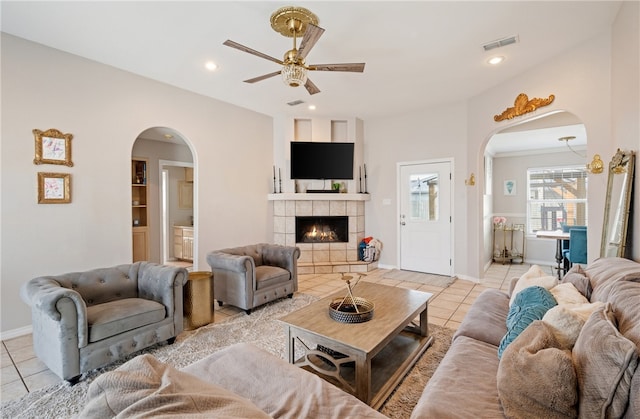 living area featuring light tile patterned floors, a fireplace, visible vents, and arched walkways