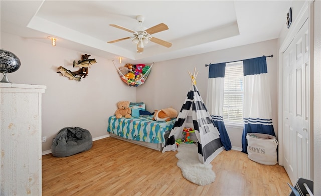 bedroom with baseboards, a closet, a tray ceiling, and wood finished floors