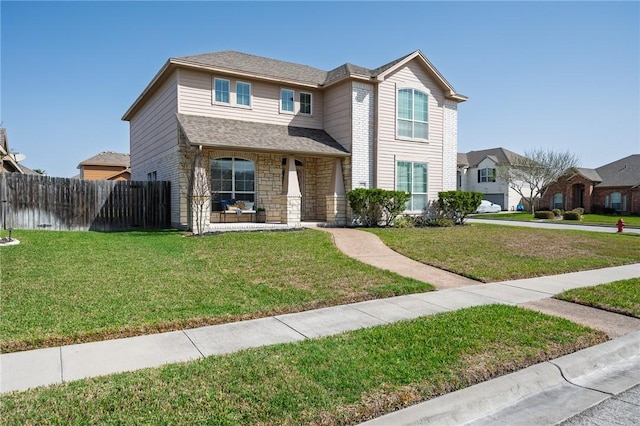 view of front of property featuring stone siding, a front lawn, a shingled roof, and fence