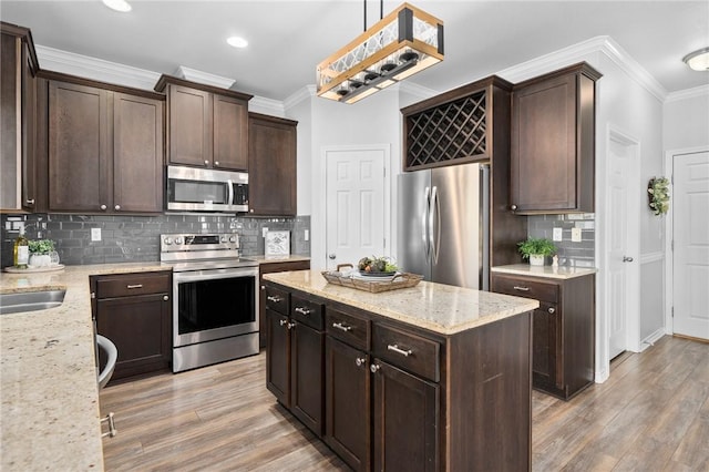 kitchen featuring dark brown cabinetry, appliances with stainless steel finishes, a center island, crown molding, and light wood-type flooring