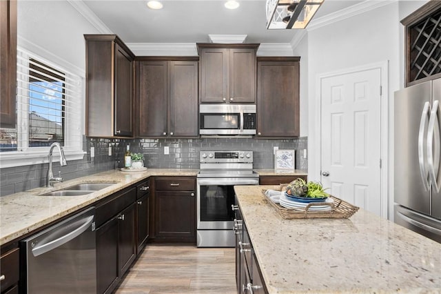 kitchen featuring stainless steel appliances, crown molding, a sink, and light stone counters