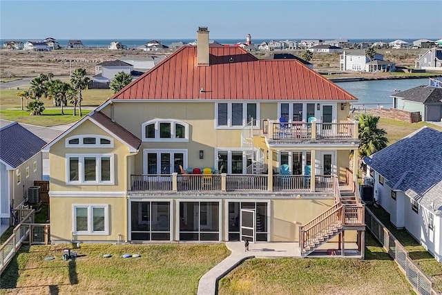 back of property featuring metal roof, a water view, stairs, a lawn, and stucco siding