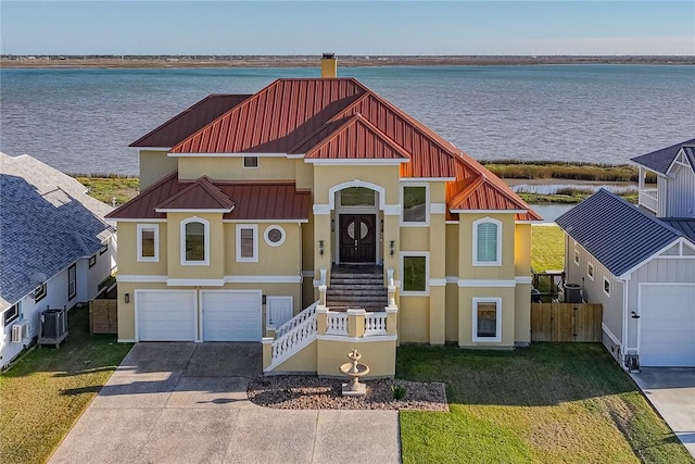 view of front of house with a standing seam roof, a water view, driveway, and metal roof