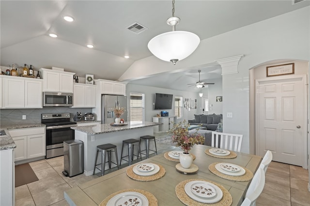 tiled dining area featuring ceiling fan, decorative columns, and vaulted ceiling