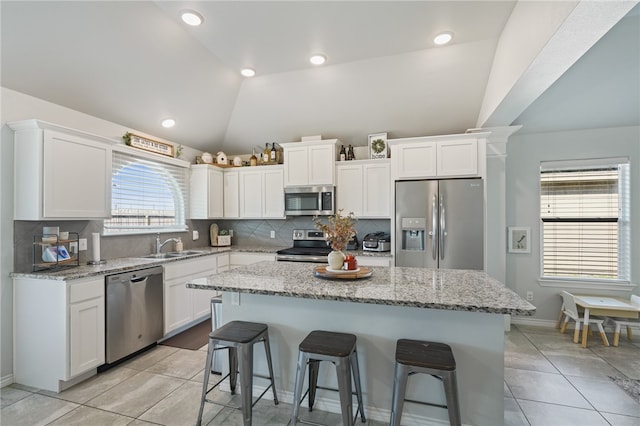 kitchen featuring appliances with stainless steel finishes, white cabinetry, vaulted ceiling, and a kitchen island