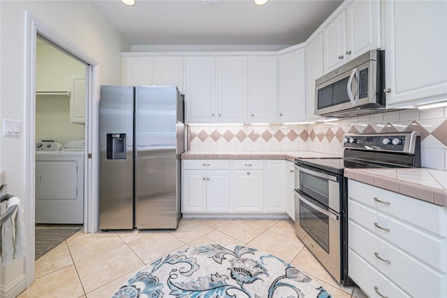 kitchen with backsplash, appliances with stainless steel finishes, tile counters, white cabinetry, and washer and clothes dryer