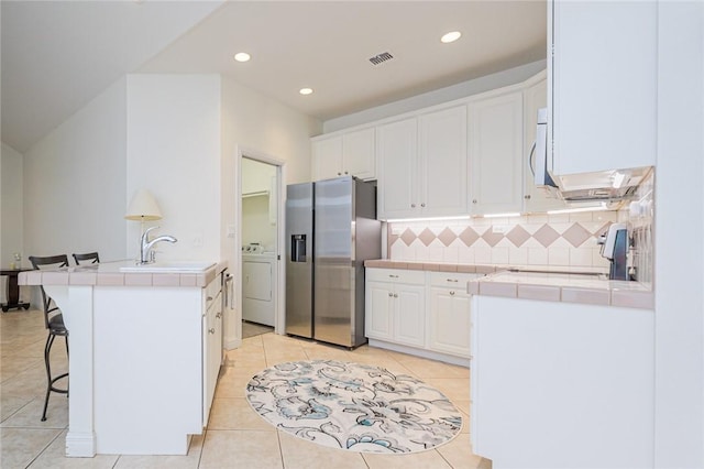 kitchen featuring stainless steel fridge, a sink, tile counters, and visible vents