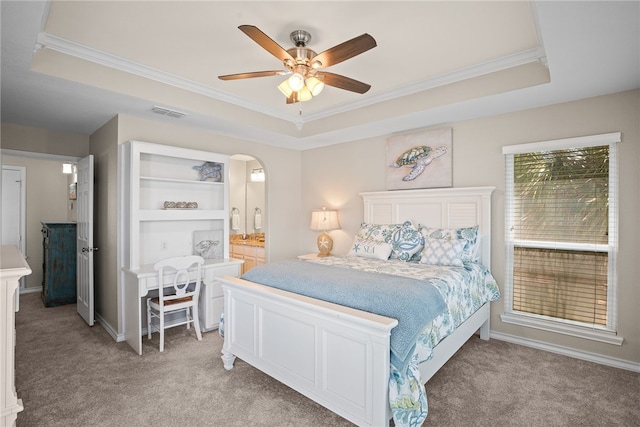 carpeted bedroom with ornamental molding, ceiling fan, ensuite bath, and a tray ceiling