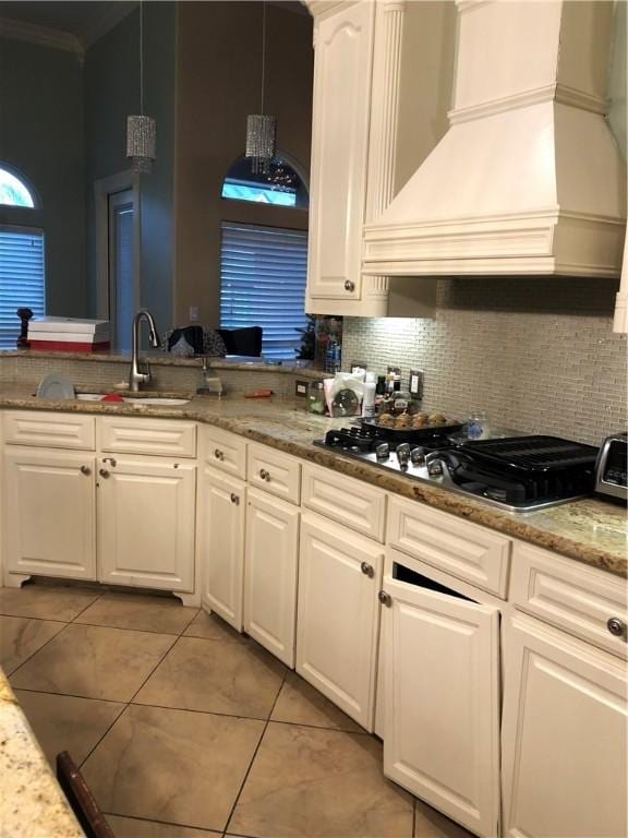 kitchen featuring light stone countertops, white cabinetry, stainless steel gas cooktop, pendant lighting, and custom exhaust hood