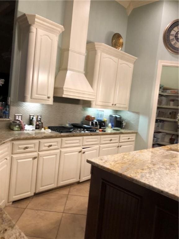 kitchen featuring stainless steel gas stovetop, custom exhaust hood, white cabinets, tasteful backsplash, and light tile patterned flooring