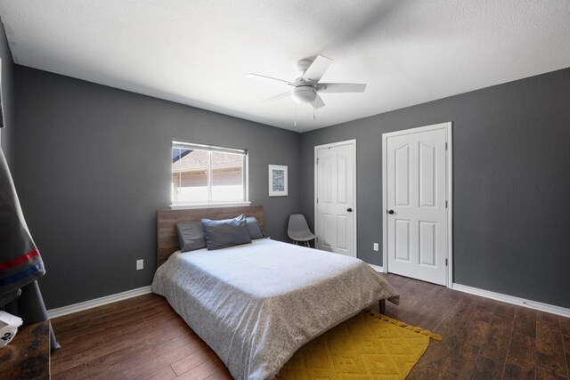 bedroom featuring a ceiling fan, baseboards, dark wood-style flooring, and two closets