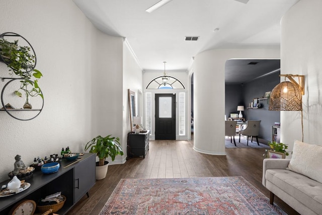 entryway featuring dark wood-type flooring, visible vents, baseboards, ornamental molding, and ornate columns