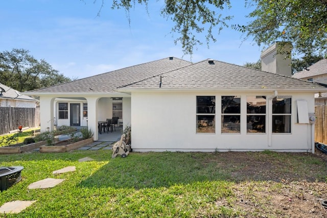 rear view of house with fence, roof with shingles, a lawn, a chimney, and a patio area