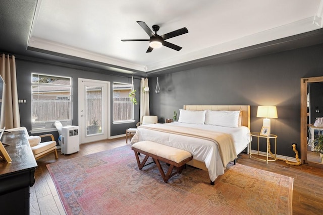 bedroom featuring access to exterior, wood-type flooring, a tray ceiling, and baseboards