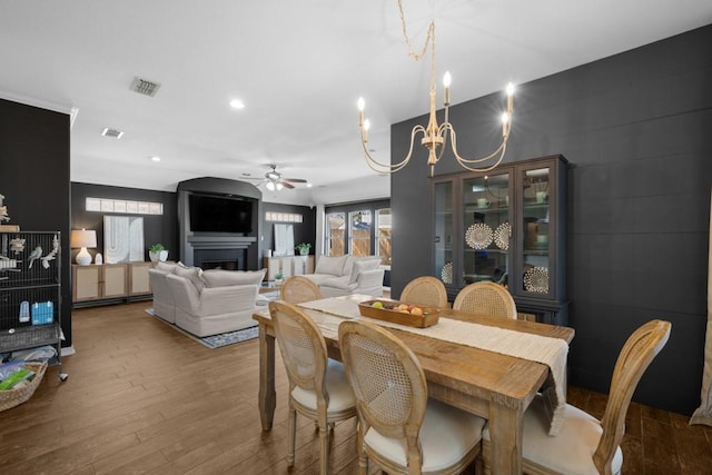 dining room featuring a fireplace, visible vents, wood finished floors, and ceiling fan with notable chandelier