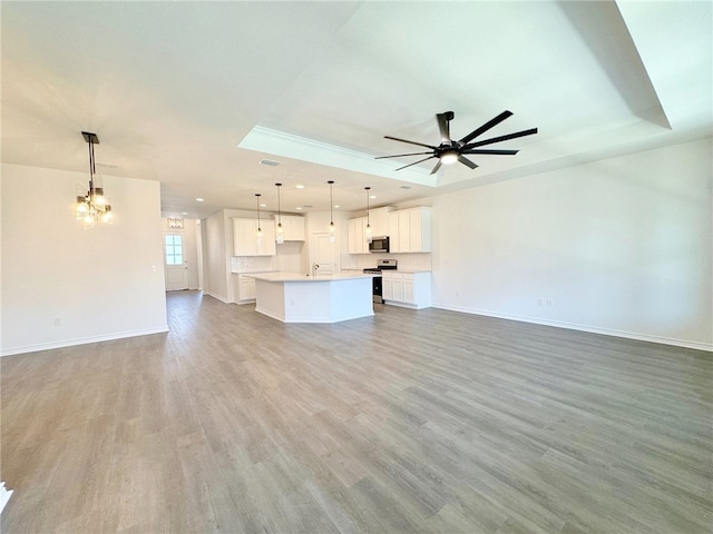 unfurnished living room with ceiling fan with notable chandelier, light hardwood / wood-style floors, and a raised ceiling