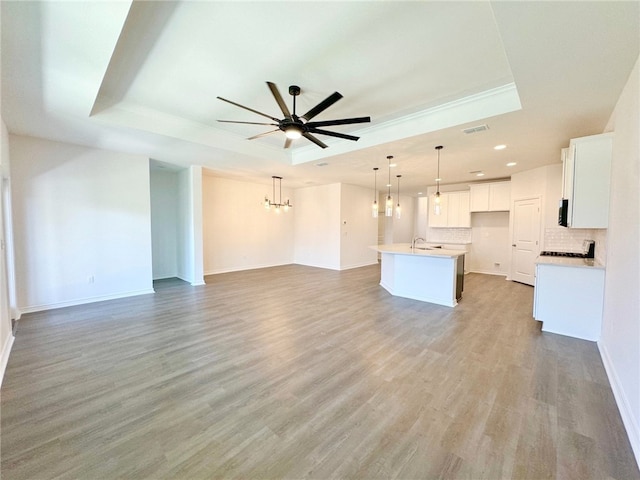 unfurnished living room with a raised ceiling, sink, light hardwood / wood-style floors, and ceiling fan with notable chandelier