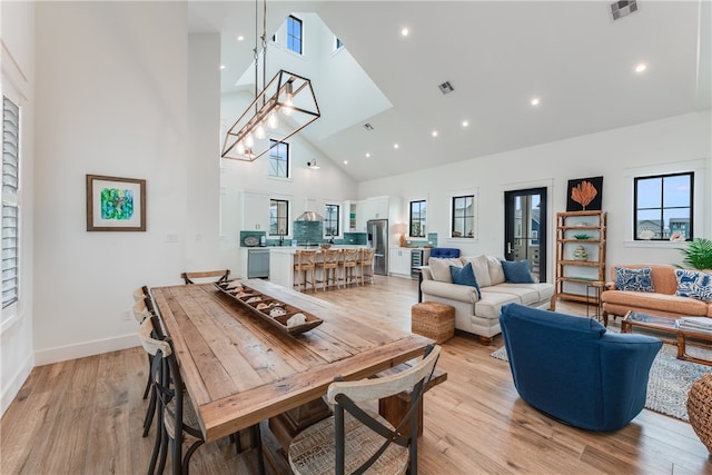 dining room featuring high vaulted ceiling, a chandelier, and light wood-type flooring