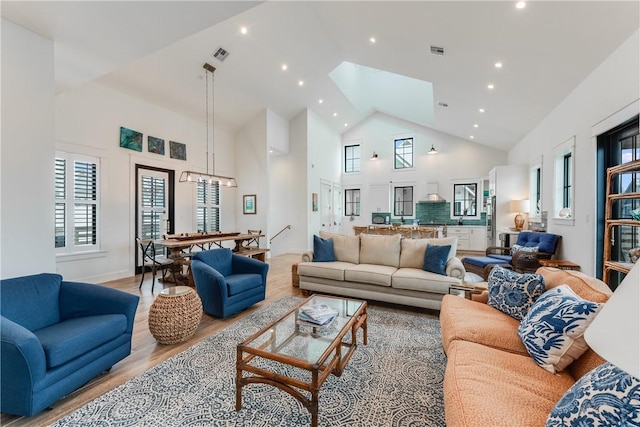 living room featuring light hardwood / wood-style flooring, high vaulted ceiling, a chandelier, and sink