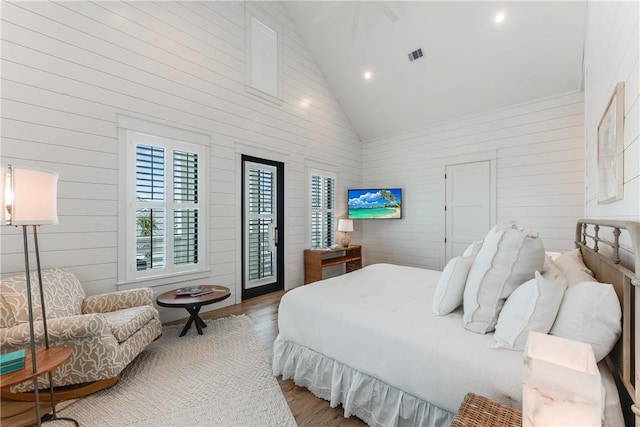 bedroom featuring access to exterior, hardwood / wood-style floors, high vaulted ceiling, and wood walls