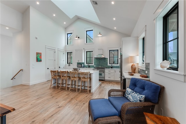 kitchen with high end range, a kitchen breakfast bar, wall chimney exhaust hood, high vaulted ceiling, and a kitchen island