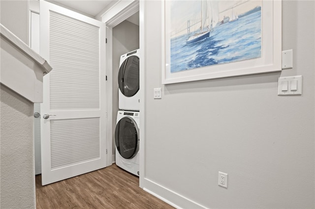 laundry area featuring laundry area, stacked washer / dryer, wood finished floors, and baseboards