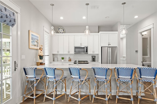 kitchen featuring a kitchen bar, backsplash, dark wood finished floors, stainless steel appliances, and light countertops