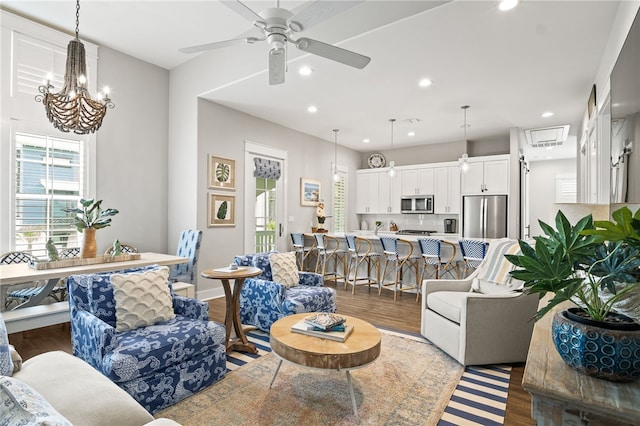 living area with ceiling fan with notable chandelier, recessed lighting, wood finished floors, and baseboards