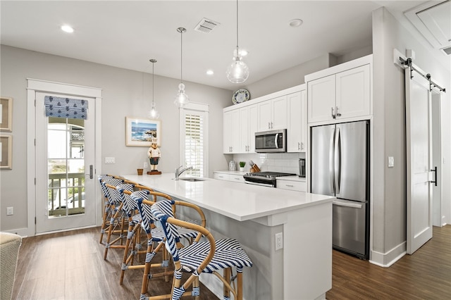 kitchen with visible vents, backsplash, dark wood-style floors, a barn door, and appliances with stainless steel finishes